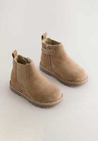 Bottines en suede marron avec une finition lisse, panneaux latéraux élastiques, une fermeture éclair et des coutures contrastées le long de la semelle. Doublure intérieure douce.