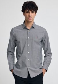 Svartvit rutig skjorta med knappar, krage, långa ärmar och en liten logotyp på bröstet; slät tygstruktur.