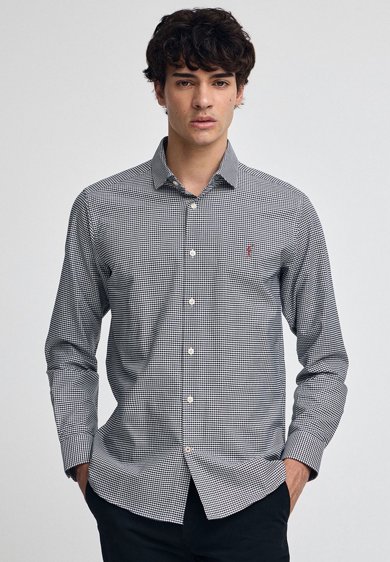 Svartvit rutig skjorta med knappar, krage, långa ärmar och en liten logotyp på bröstet; slät tygstruktur.