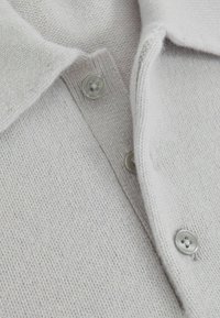 Maglione grigio chiaro lavorato a maglia con una texture morbida, caratterizzato da un collo a camicia e tre bottoni rotondi e trasparenti lungo la parte anteriore.