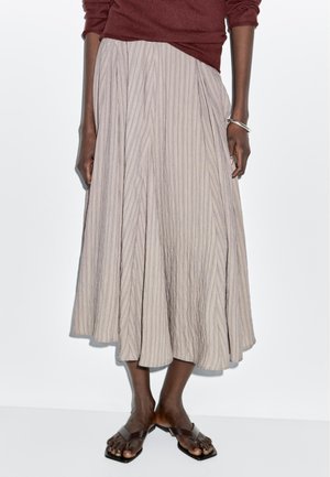 Lång, plisserad kjol i ljusgrått med vertikala ränder och en flödande design. Kombinerad med enkla bruna platta sandaler.