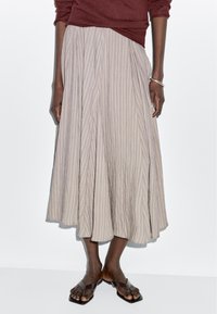 Lange, geplooide rok in lichtgrijs met verticale strepen en een vloeiend design. Gecombineerd met eenvoudige bruine platte sandalen.