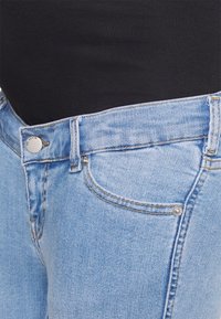 Jeans de ganga azul claro com um corte clássico. As características incluem um fecho de botão prateado, bolsos frontais e costura em contraste.