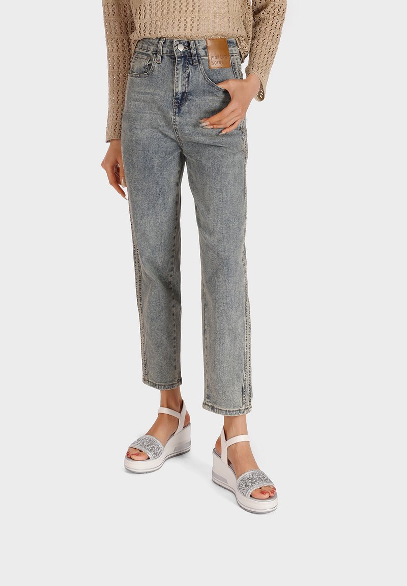 Jeans blu chiaro a vita alta in denim, con taglio dritto e cuciture a vista. Abbinati a sandali con zeppa bianchi con accenti scintillanti.