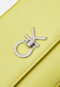 Clutch in pelle gialla con un evidente chiusura in tonalità argento con design del logo, texture liscia e dettagli di cucitura sui bordi.