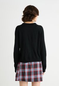 Pulover negru tricotat cu guler rotund și mâneci lungi, asortat cu o fustă mini în carouri, având culori roșu, albastru și gri.