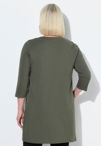 Olivgrön tunika med trekvartslånga ärmar, tillverkad av mjukt tyg. Har en rundad halsringning och en avslappnad passform som sträcker sig nedanför höfterna.