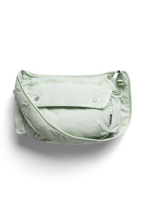 Sac bandoulière matelassé vert clair avec rabat à l'avant fermé par deux boutons-pression et bandoulière ajustable sur fond blanc.