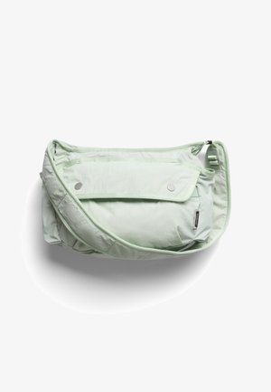 Sac bandoulière matelassé vert clair avec rabat à l'avant fermé par deux boutons-pression et bandoulière ajustable sur fond blanc.