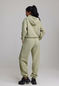 Mikina a nohavice z fleece v svetlo zelenej farbe s kapucňou, má elastické manžety a pás. Doplněné čiernými športovými topánkami. Viditeľný textúrovaný povrch.