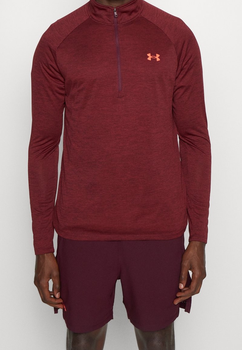 Maroon långärmad atletisk tröja med halvmeterdragkedja och raglanärmar. Har Under Armour-logotyp i orange på bröstet.