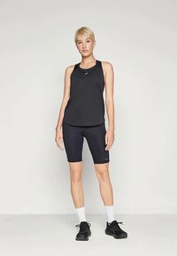 Melnas sporta kreklas bez piedurknēm un riteņbraukšanas šorti, pieguļošs dizains, gluda tekstūra, ar logotipa detaļu, saskaņots ar baltām zeķēm un melniem sporta apaviem.