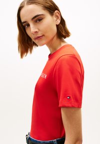 Maglietta rossa in cotone con maniche corte, con logo bianco e piccolo dettaglio con bandiera sulla manica sinistra. Vestibilità semplice e classica.