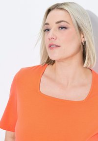 Top de manga corta y escote cuadrado en tejido de un vibrante color naranja. Textura suave con líneas limpias y detalles de costura mínimos.