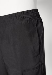 Bermudas negras con una cinturilla elástica, con una textura suave y un bolsillo lateral. Diseño sencillo sin patrones o acentos adicionales.