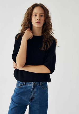 Svart stickad tröja med kort ärm, med rund halsringning. Bärs med högmidjade blåjeans. Enkelt design, mjuk textur.