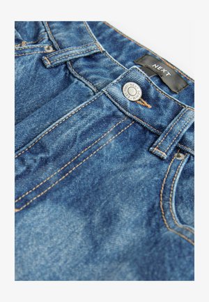 Mėlynos džinsinės kelnės su matomu siuvimu, priekyje esančiu mygtukų užsegimu ir logotipo etikete ant juosmens. Audinys atrodo nudėvėtas.