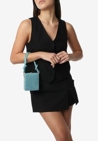 Piccola borsa quadrata in turchese con un esterno texturizzato ricoperto di strass. Presenta una maniglia intrecciata annodata e dettagli in hardware argentato.
