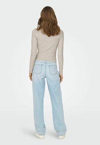 Jeans a gamba larga blu chiaro con vita alta, dotati di tasche posteriori e texture morbida, abbinati a un top fitted beige a maniche lunghe.