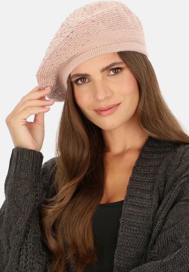 Jasnoróżowa dzianinowa beretka o teksturowanym wzorze i subtelnym połysku. Noszona w lekko przechylonej pozycji, uzupełniona ciemnoszarym dzianinowym kardiganem.