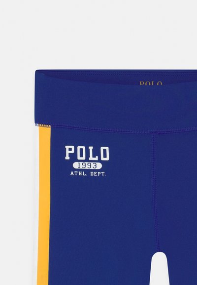 Leggings desportivos azuis com o texto branco "POLO 1993 ATHL. DEPT.", com riscas de destaque amarelas nas laterais e um tecido liso e elástico.