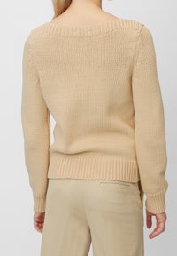 Pull beige en tricot avec un large décolleté, des poignets et un ourlet côtelés. Le tissu présente un motif texturé, offrant une coupe décontractée.