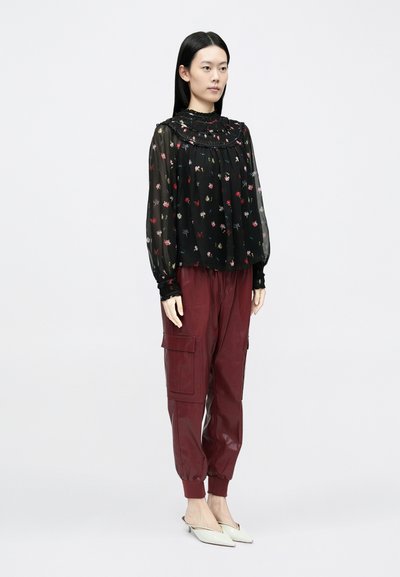 Blusa nera a fiori con maniche lunghe e colletto arricciato, abbinata a pantaloni cargo aderenti bordeaux e ballerine crema con punta a punta.