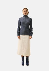 Marineblauer, gerippter Rollkragenpullover mit langen Ärmeln, kombiniert mit einem cremefarbenen Rock und glänzenden blauen Knöchelstiefeln mit rechteckigem Absatz.