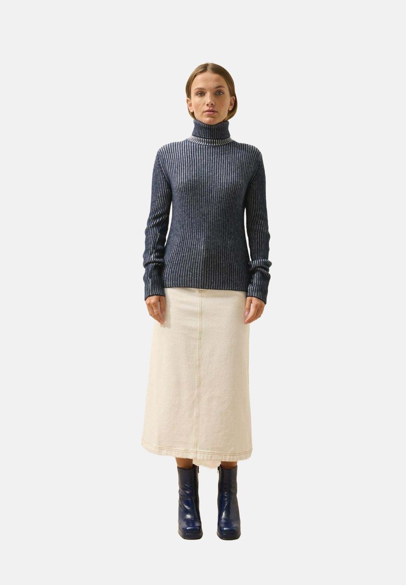 Marineblauer, gerippter Rollkragenpullover mit langen Ärmeln, kombiniert mit einem cremefarbenen Rock und glänzenden blauen Knöchelstiefeln mit rechteckigem Absatz.