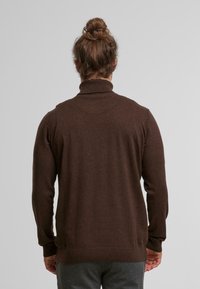 Brauner Strickpullover mit hohem Kragen, gerippten Bündchen und Saum sowie einer glatten Textur. Besitzt ein tailliertes Design mit einer Rückennähten.