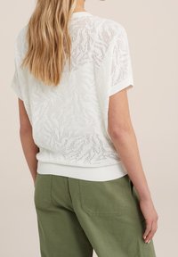 Pull blanc à manches courtes avec un motif texturé et ajouré ; ourlet côtelé. Assorti à un pantalon olive avec des poches à rabat.