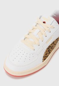 Sneaker bianco con punta perforata, lacci beige e pannello laterale con un design a stampa leopardata. Suola in gomma con un accento rosa.
