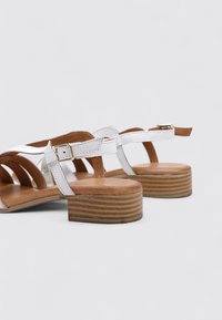 Sandales en cuir blanc avec plusieurs brides, fermeture à boucle et talon en bois. Semelle intérieure texturée avec des accents brun clair.