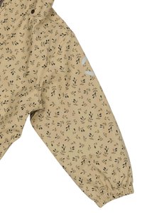Manica di giacca beige con un motivo foglioso in verde e nero. Presenta polsini elasticizzati e una texture di tessuto morbido e leggero.