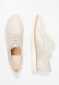 Chaussures en cuir beige avec une finition texturée et scintillante, dotées d'un design à lacets et d'une semelle blanche striée pour une meilleure adhérence et un confort optimal.