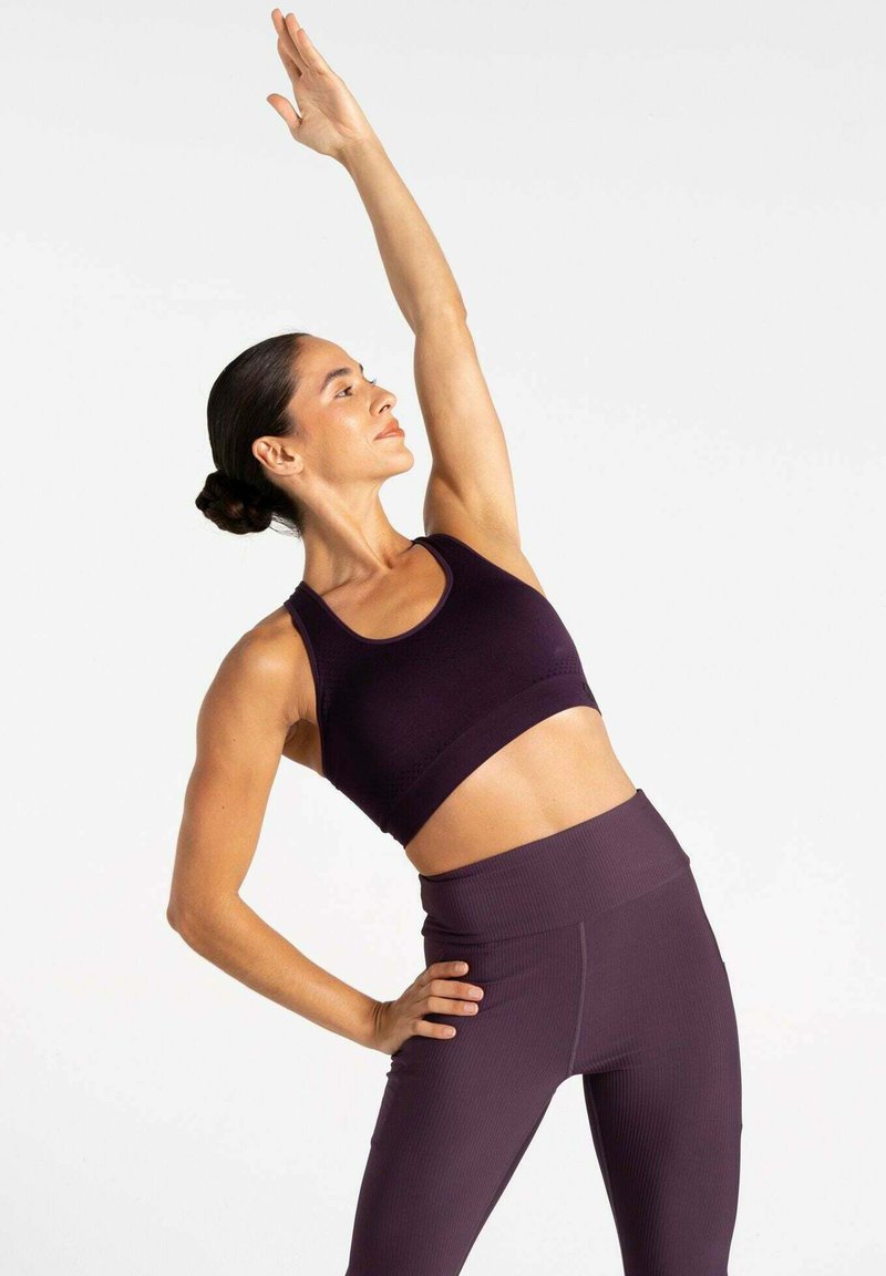 Lila Sport-BH und hochtaillierte Leggings aus geripptem Stoff. Modell streckt einen Arm nach oben, um die Passform und das Design des Outfits zu zeigen.