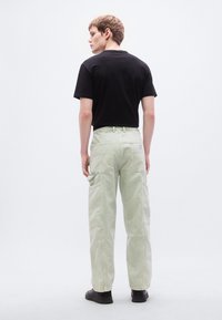 Ανοιχτοπράσινο παντελόνι εργασίας με πολλαπλές πλαϊνές τσέπες και ίσια γραμμή, συνδυασμένο με εφαρμοστό μαύρο μπλουζάκι. Μινιμαλιστικός σχεδιασμός.