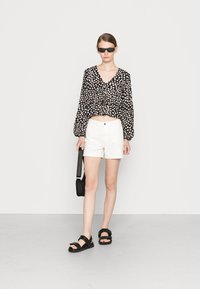 Blusa com padrão preto e branco, com mangas volumosas, combinada com calções brancos. Sandálias pretas e uma pequena bolsa preta complementam o visual.
