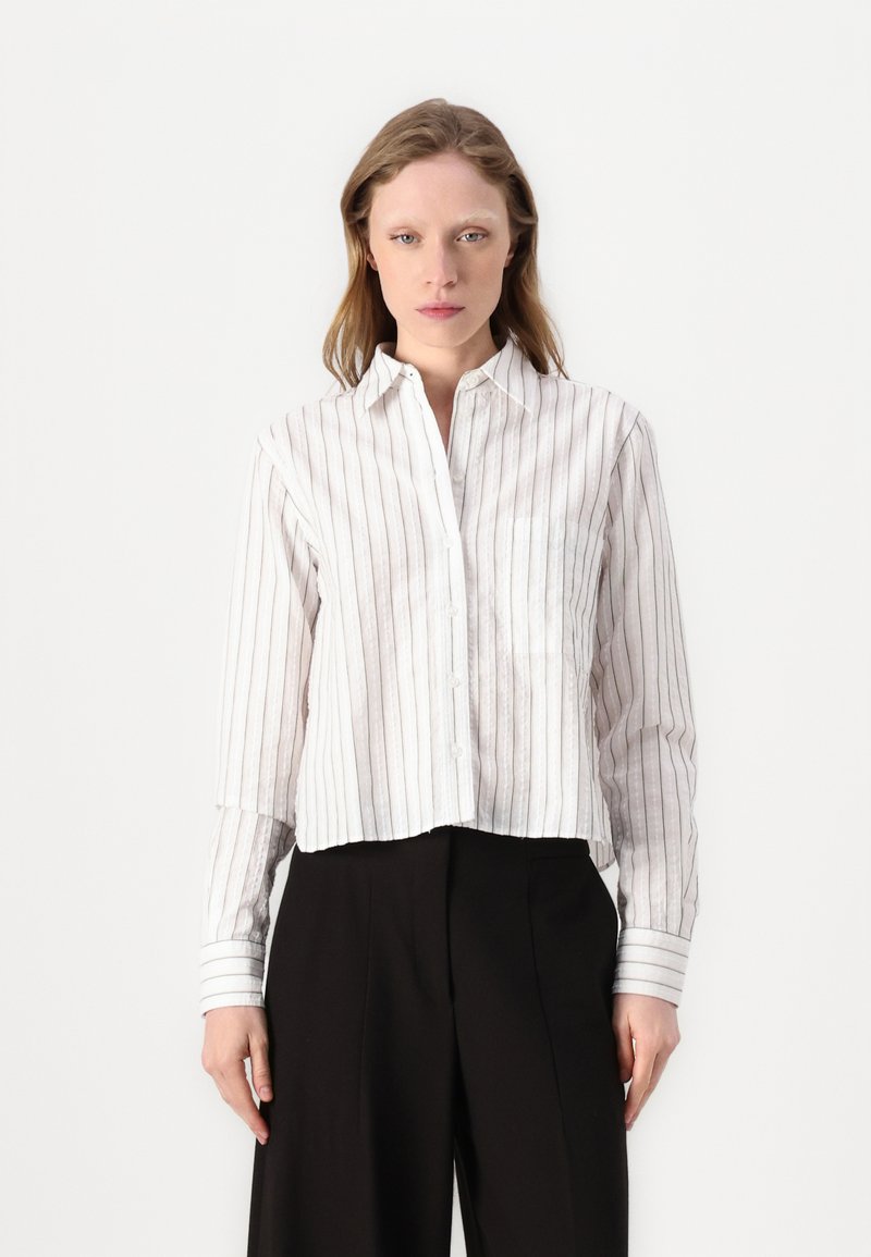 Camicia bianca a righe con bottoni, caratterizzata da maniche lunghe, colletto a punta e un design corto con una finitura texturizzata.