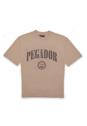 Beige cotton t-shirt with short sleeves, featuring "PEGADOR" printed in bold black letters and a circular graphic design below.