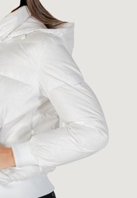 Giacca a vento bianca, con cappuccio, polsini a costine e un'etichetta logata sulla manica. Tessuto liscio e lucido con motivo a trapunta.