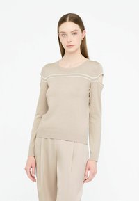 Beige Strickpullover mit rundem Halsausschnitt, Schulterauschnitten und weißen horizontalen Linien über der Brust; gerippter Saum und Bündchen.