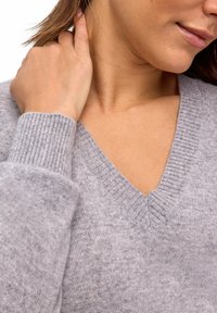 Hellgrauer V-Ausschnitt-Pullover mit gerippten Bündchen und Ausschnitt, aus einem weichen Material gefertigt, mit lockerer Passform und minimaler Textur.