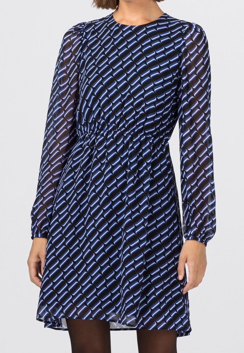 Modrá šaty s vzorem, dlouhými průhlednými rukávy, shromážděným pasem a splývavou sukní, s geometrickým designem v světlé modré na tmavém pozadí.