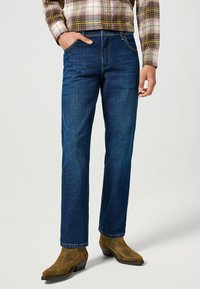 Vaqueros de denim azul oscuro con un diseño de pierna recta, que cuentan con dos bolsillos frontales y detalles de costura sutil a lo largo de las costuras.