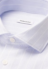 Camicia a righe blu chiaro con tessuto a trama, bottoni bianchi e colletto a punta. L'etichetta recita "seidensticker." Finitura superficiale liscia.