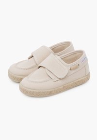 Scarpe slip-on beige in tela con strap in velcro, suola testurizzata simile a juta e dettagli di cucitura lungo la parte superiore. Design leggero e informale.