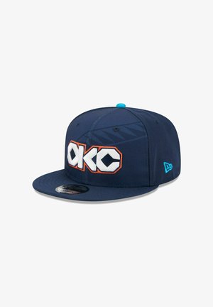 Marineblaue Baseballkappe mit flachem Schirm, vorne mit weißer und oranger "OKC"-Stickerei und einem türkisfarbenen Knopf oben. Strukturierter Stoff.