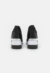 Svarte atletiske joggesko med mesh-overdel, sølvfarget aksent på hælen, svart logomerke og hvit mellomsåle. Slip-on-design med glidelåser.