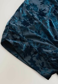 Velvet dress in dark teal featuring a floral pattern with raised texture. Smooth fabric finish and elegant drape enhance its visual appeal.